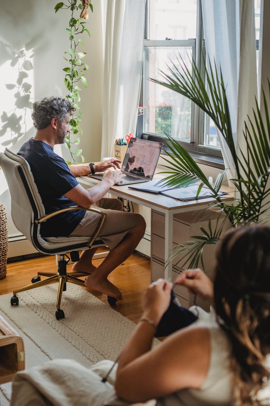 adult man working at home while wife knitting